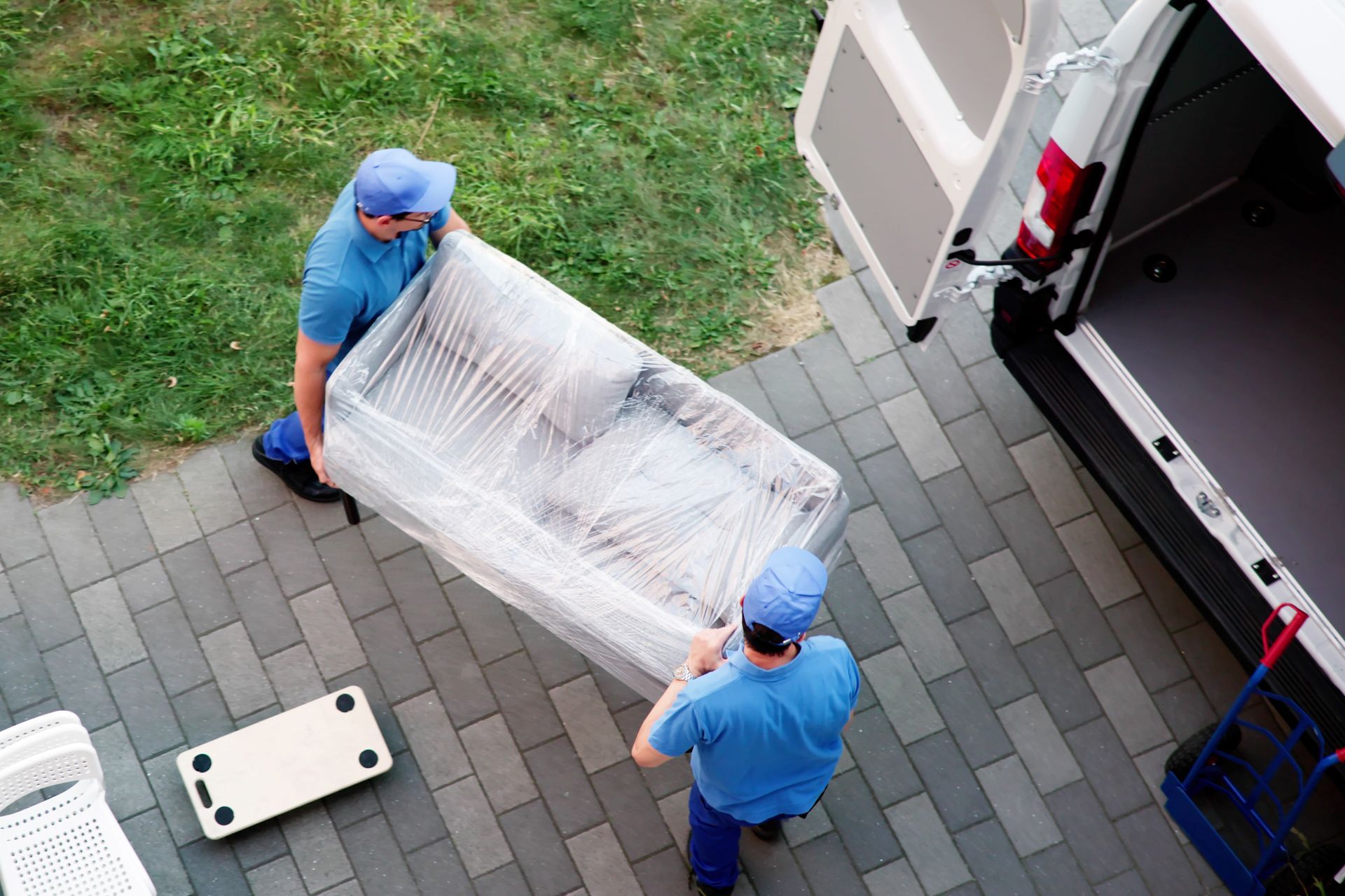 Specialists in blue uniforms are performing furniture removal, moving a sofa into a truck. Specialists in blue uniforms are performing furniture removal, moving a sofa into a truck.