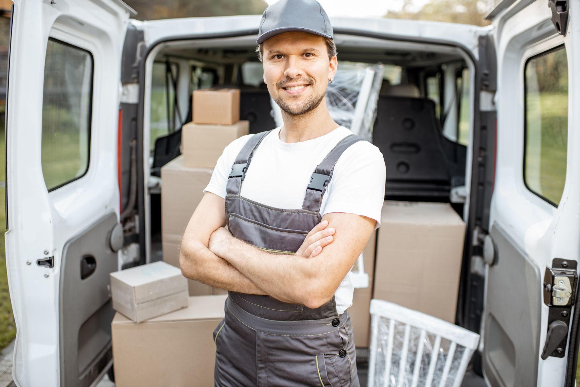 Smiling removalist standing in front of open van loaded with moving boxes and furniture.