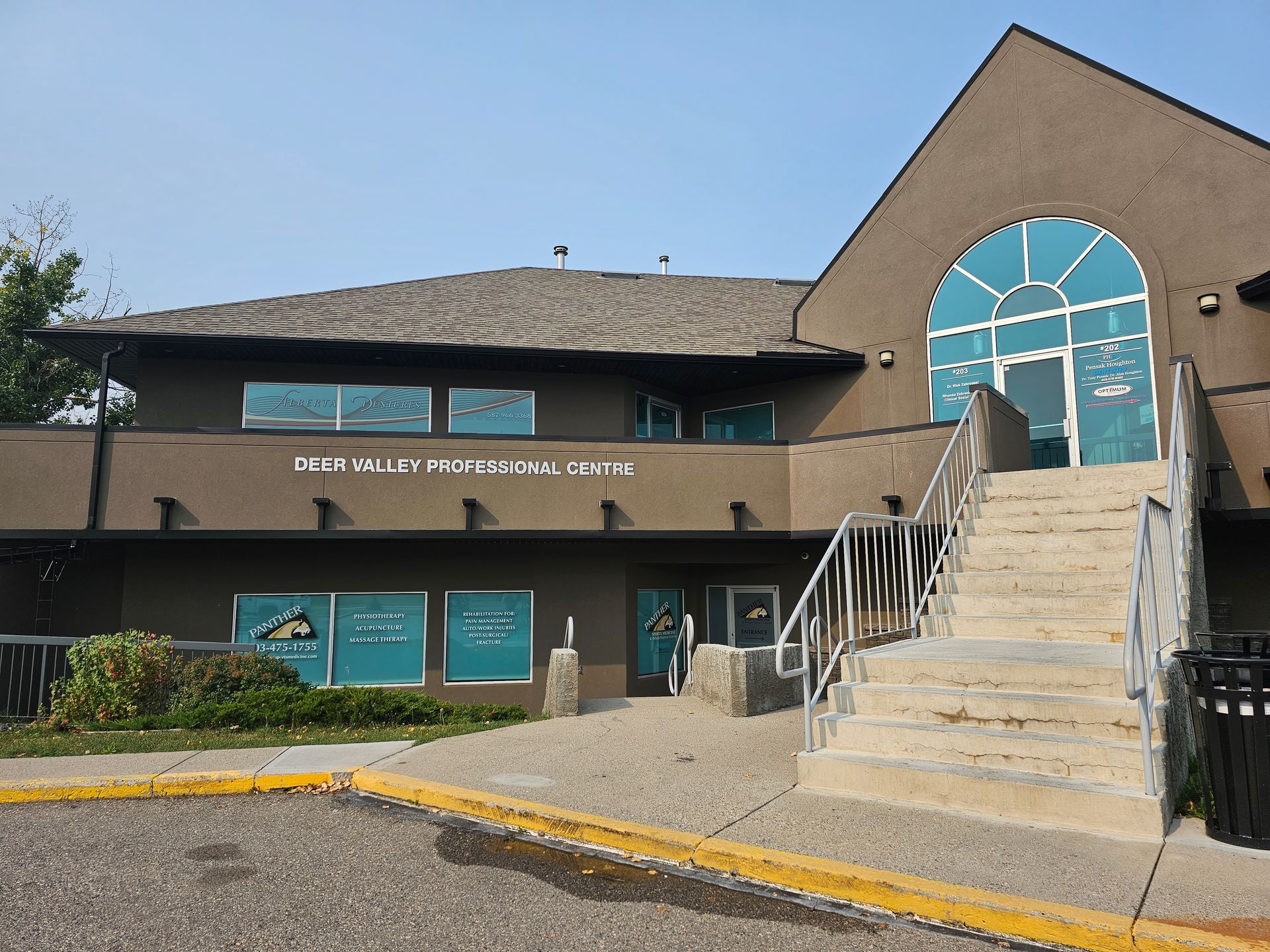 Exterior of a brown building with stairs and arched blue-glass entrance under a clear sky