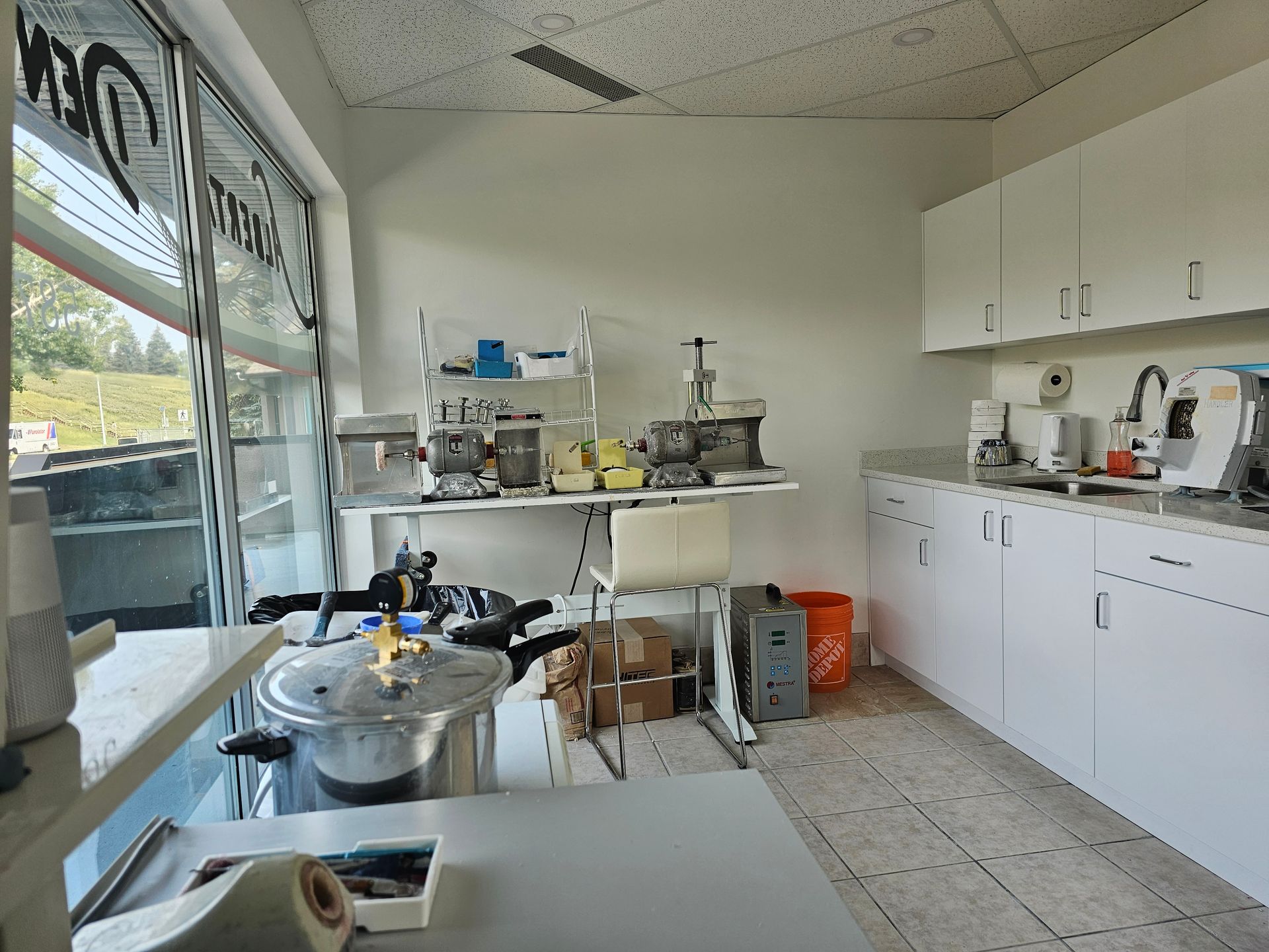 Small commercial kitchen with prep tables, stainless equipment, white cabinets, and a front window.