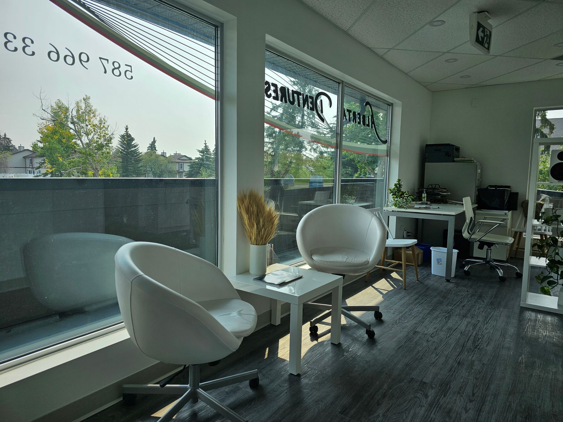 Modern salon waiting area with white chairs, tables, and large windows overlooking greenery