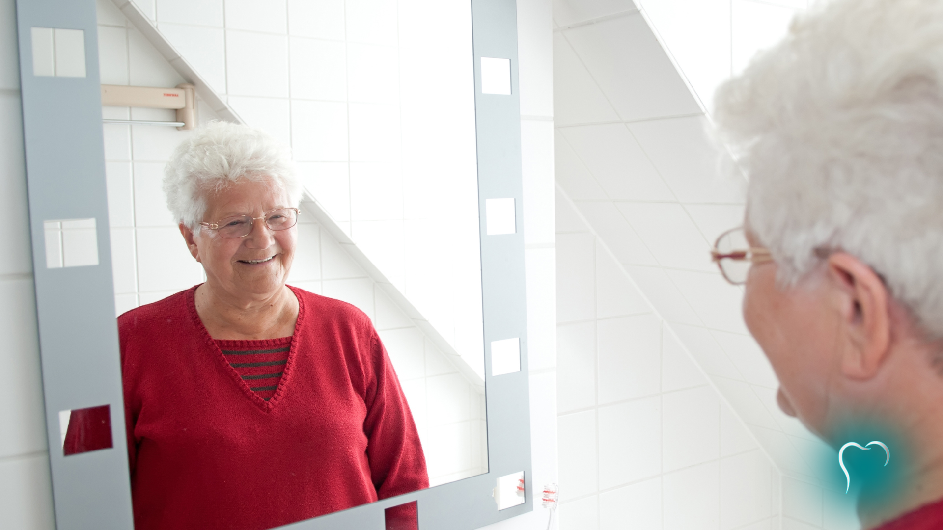 Elderly woman in a red sweater looking at her reflection in a bathroom mirror