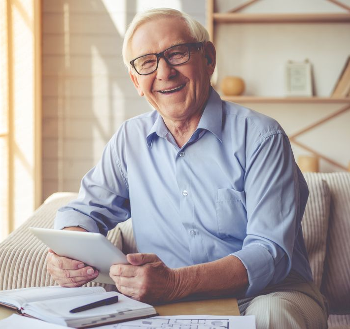 Smiling man in glasses holding a tablet in a sunlit living room