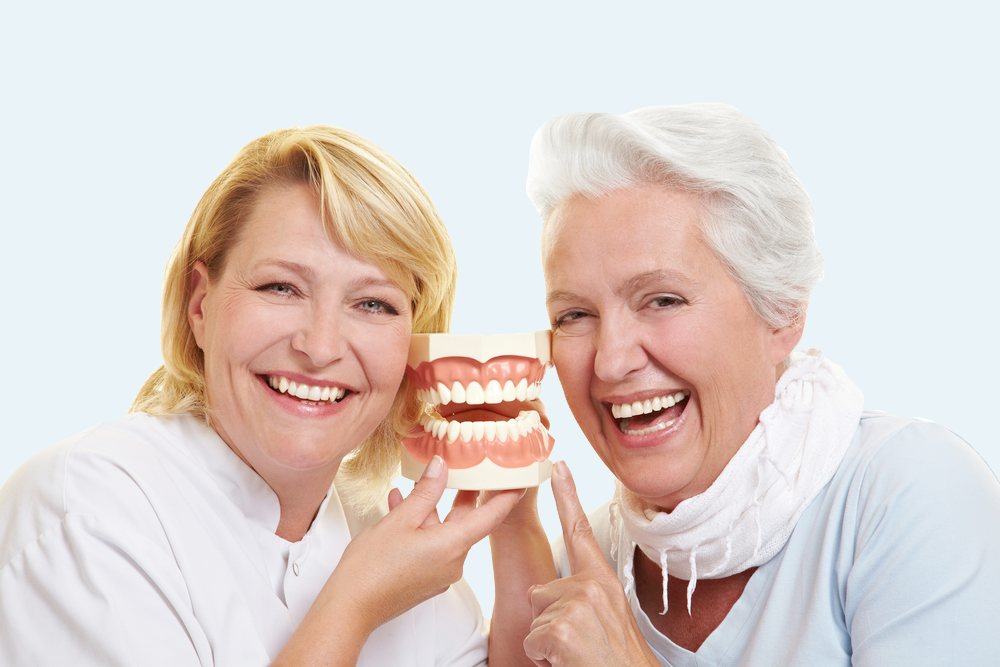 Two smiling people in white coats holding a dental model against a light background