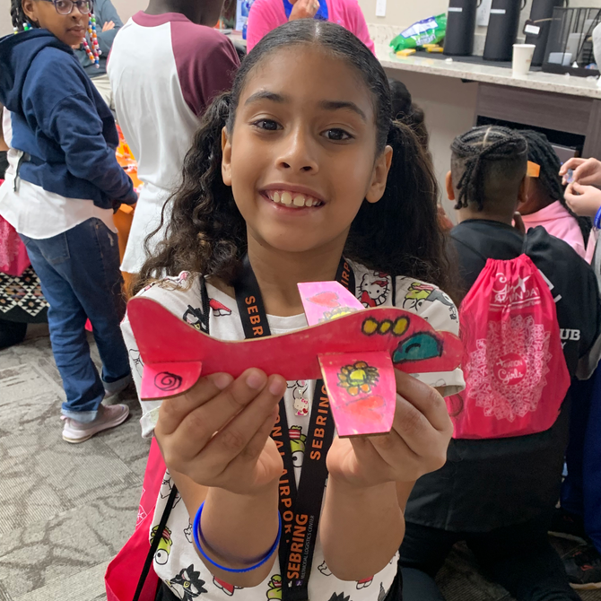 Girl smiling and holding a pink paper craft in a classroom setting