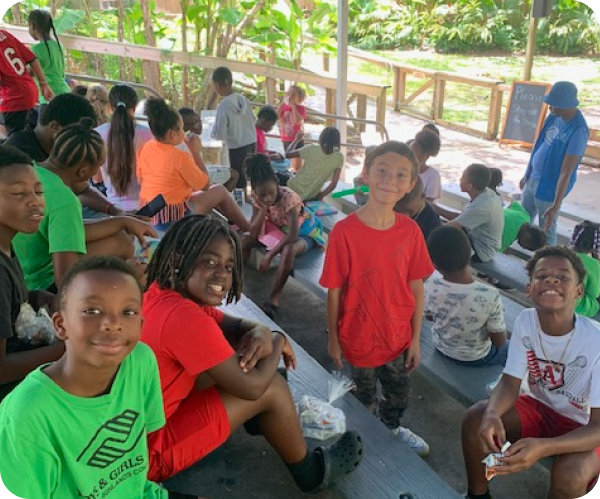 Children gathered on a covered outdoor bench, smiling and looking at the camera.