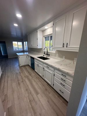 Long galley kitchen with white cabinets, gray wood floors, and a window over the sink.
