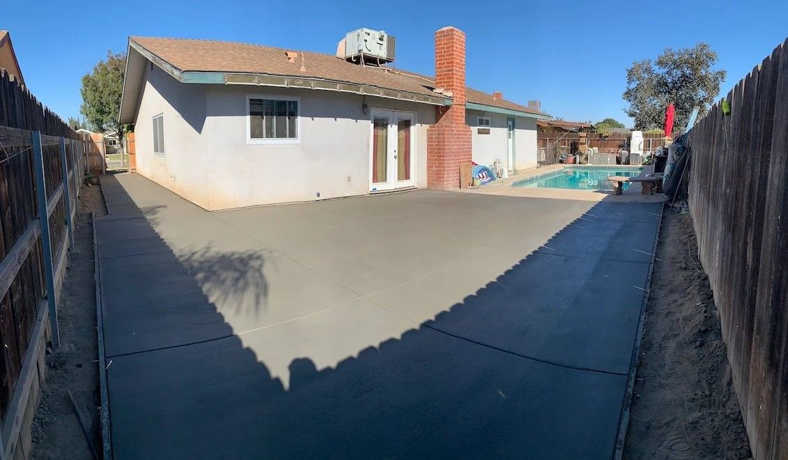 Concrete driveway leading to a single-story house with a tiled roof and fenced sides on a sunny day