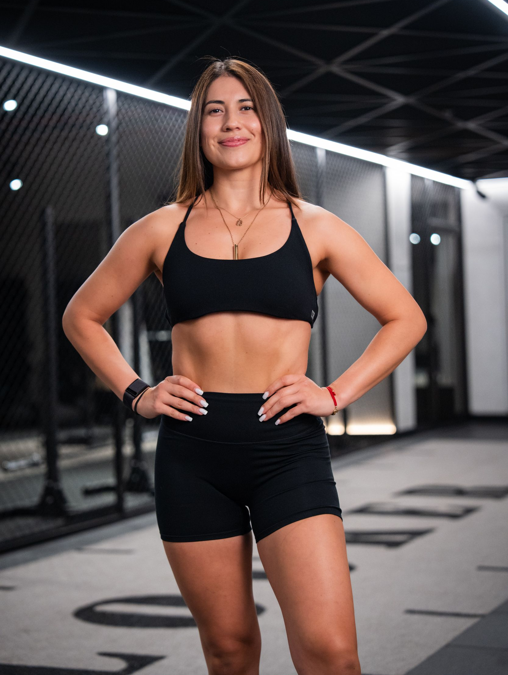 A woman is holding a dumbbell in a gym and smiling.
