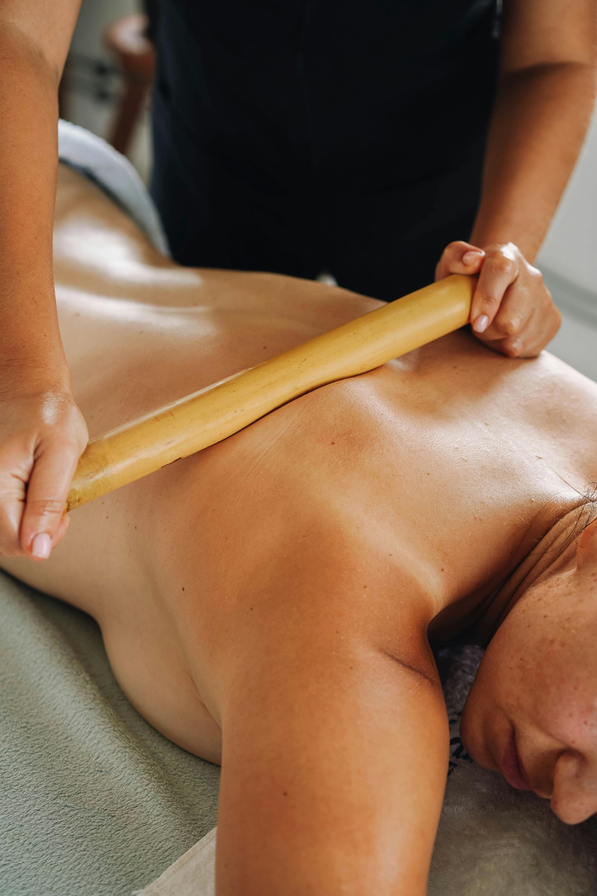 Person receiving bamboo massage on their back in spa-like setting.