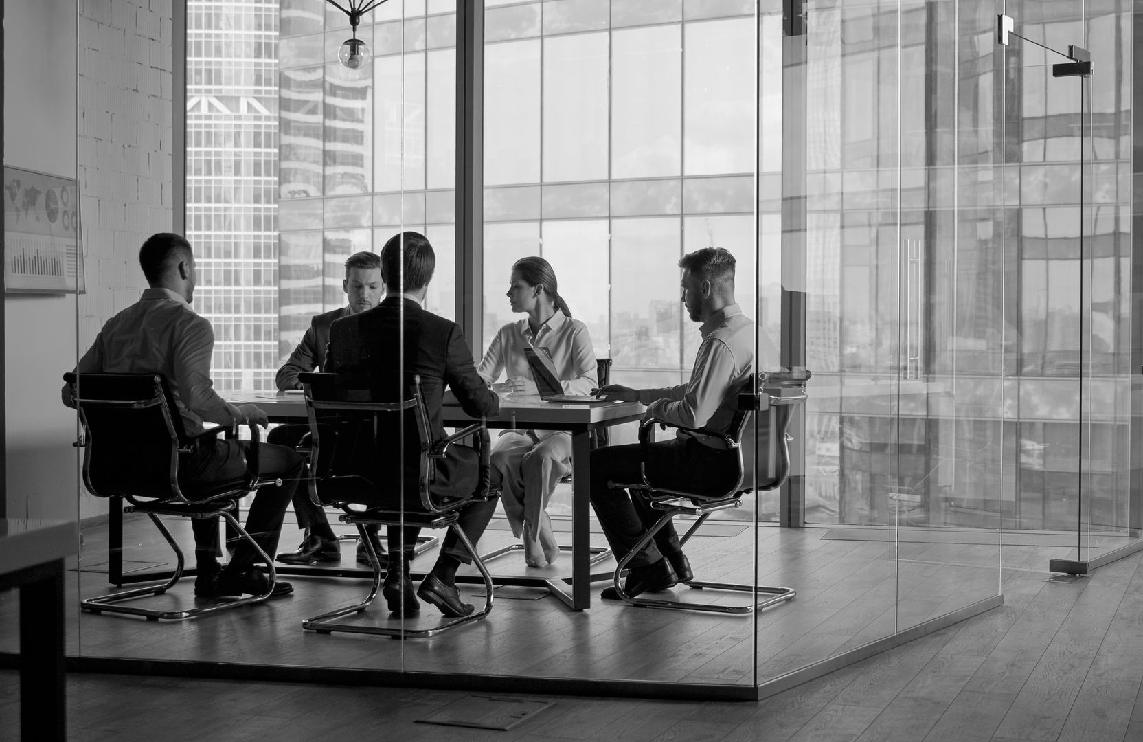 Vier Personen unterhalten sich in einem gläsernen Besprechungsraum an einem Tisch in einem modernen Büro.