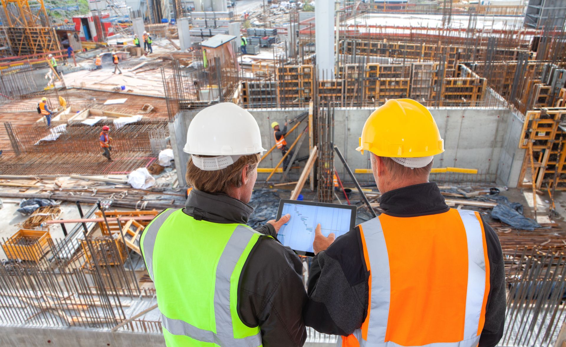 Two construction workers in hard hats reviewing a site plan at an active construction site.