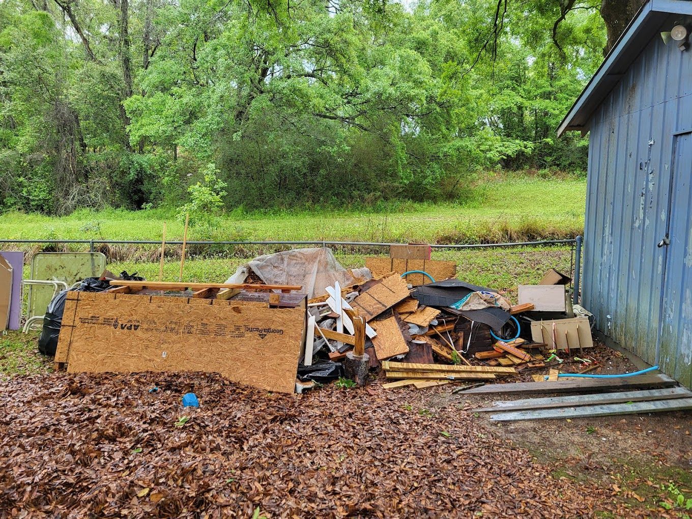 A pile of trash is sitting in front of a blue shed.