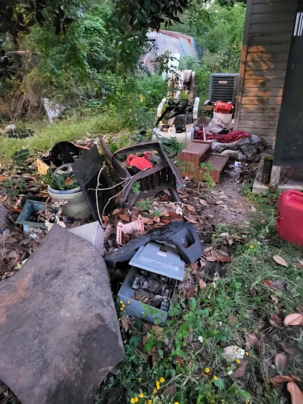 A pile of trash is sitting in the grass in front of a house.
