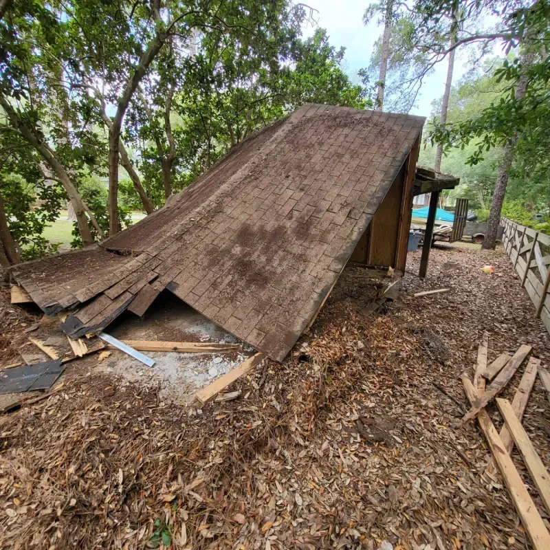 A shed with a roof that has fallen over is sitting on top of a pile of leaves.