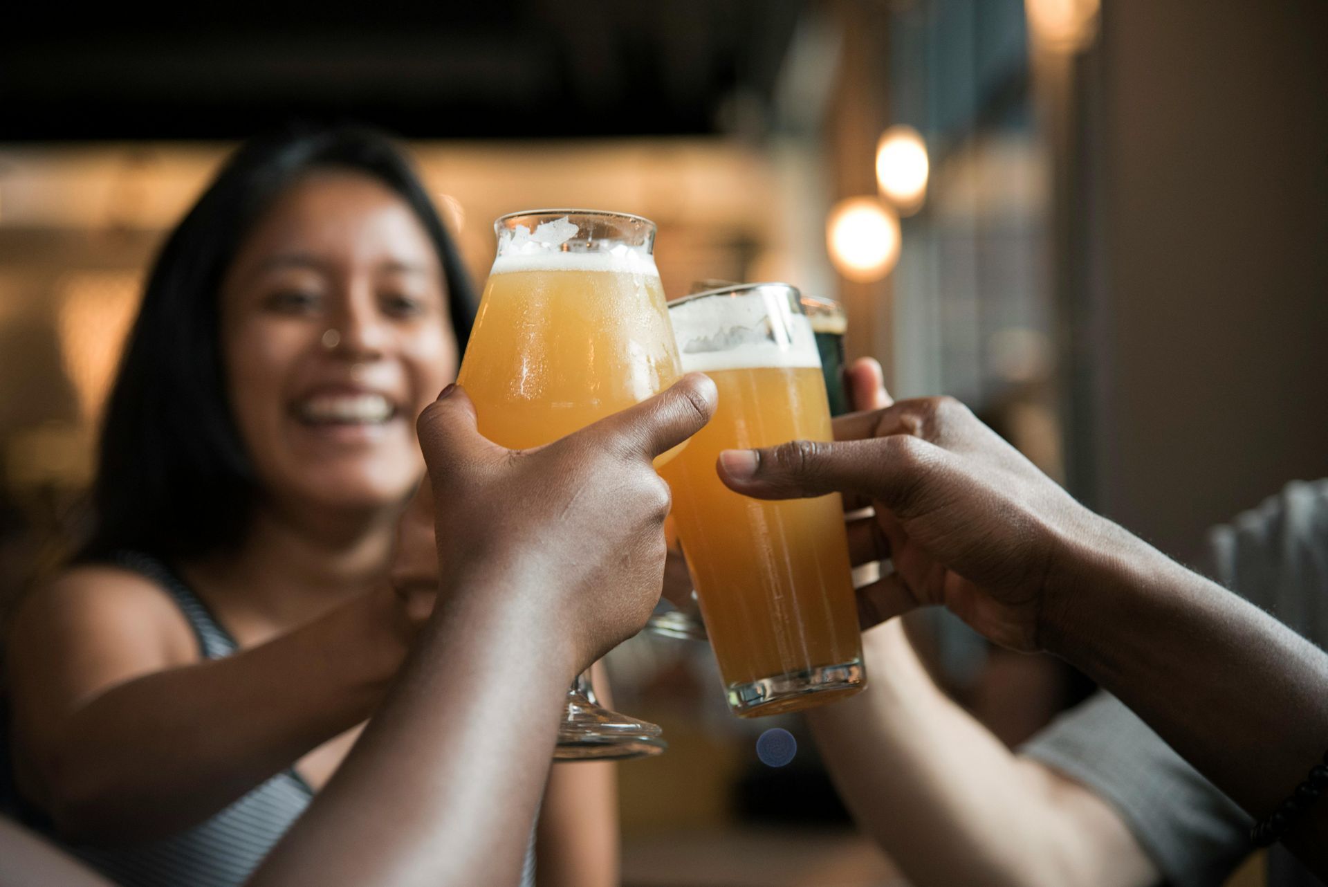 People toasting with beer glasses. Woman smiling in background.