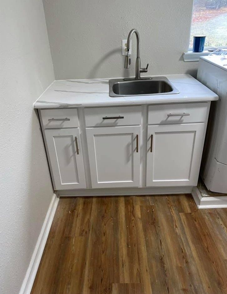 A laundry room with a sink , cabinets , and hardwood floors.