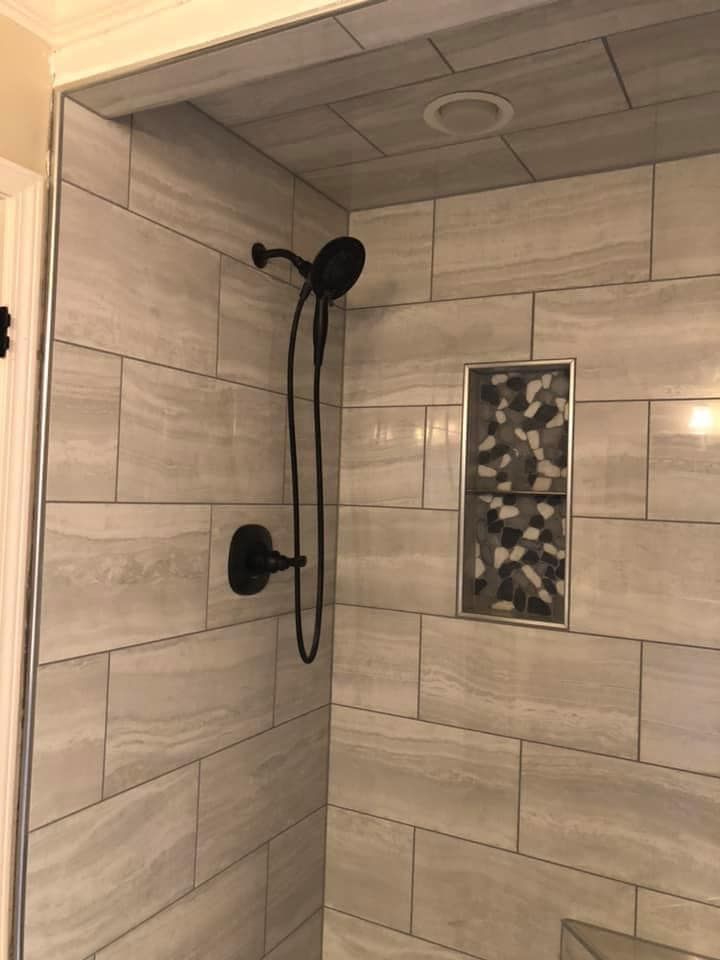 A shower with a black shower head and a tiled wall.