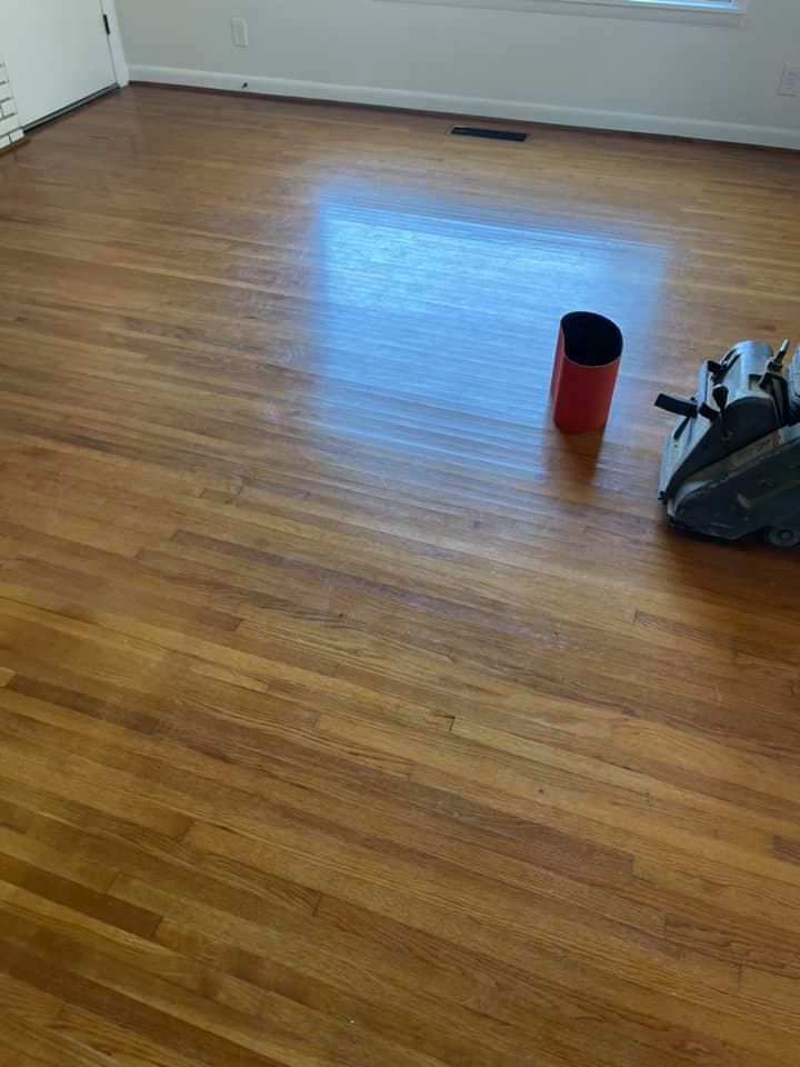 A wooden floor with a vacuum cleaner and a red bucket on it.