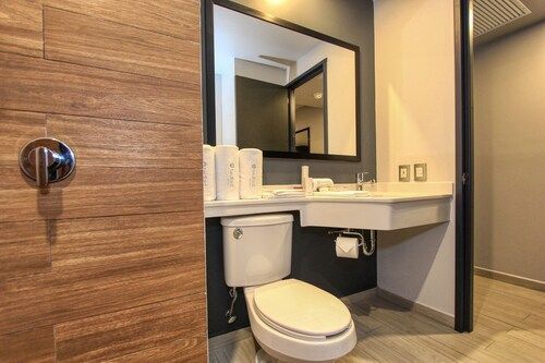 Baño con pared con textura de madera, inodoro, lavabo, espejo y zona de lavabo accesible.