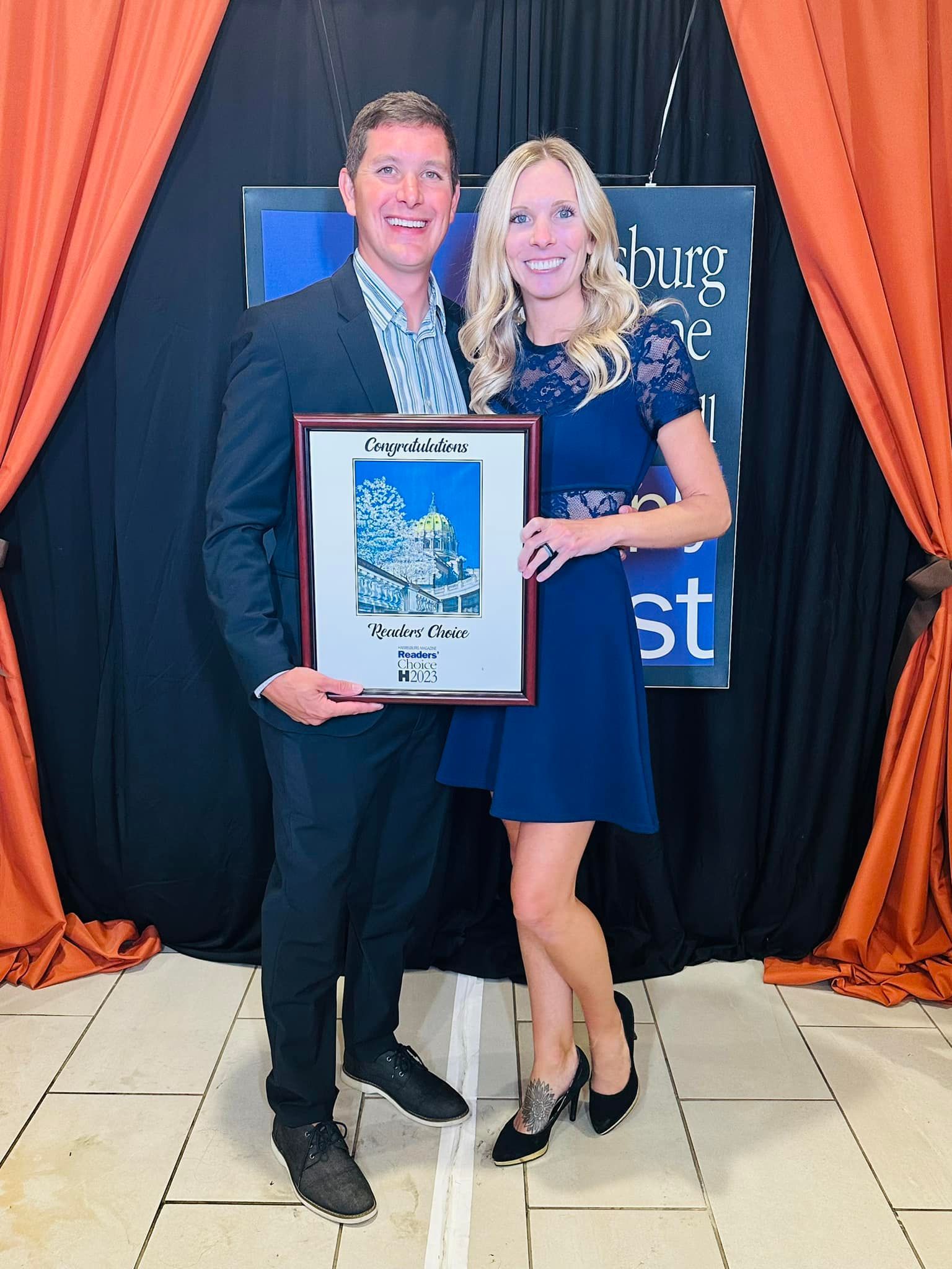 A man and a woman are posing for a picture while holding a framed picture.