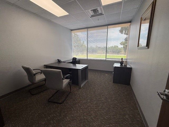 A small office with a desk , chairs and a window.