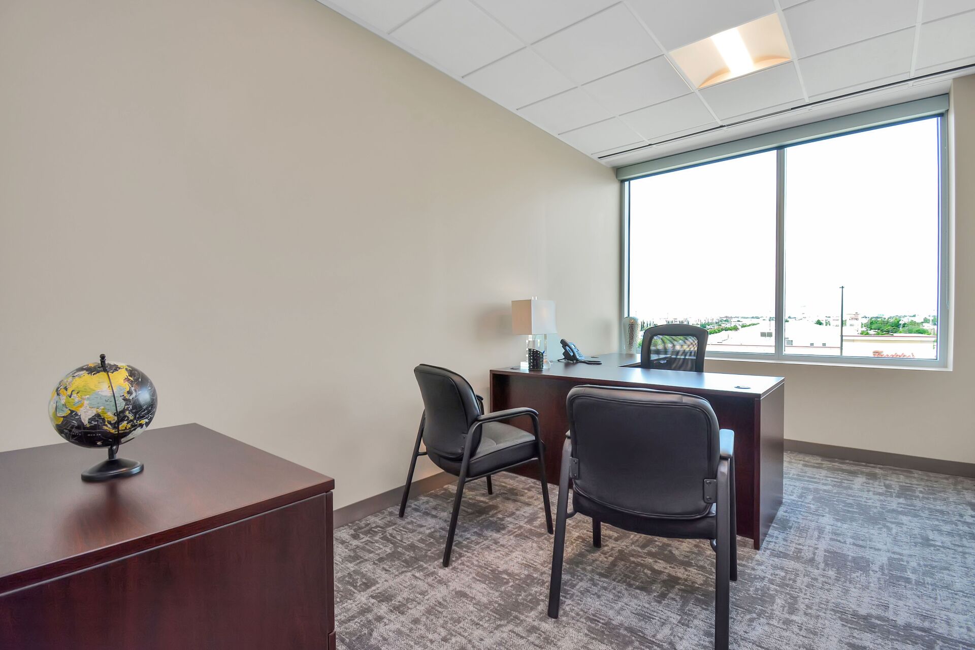 A small office with a desk , chairs and a window.