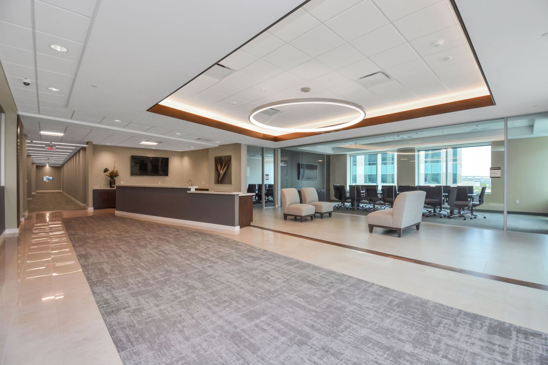 A large lobby with a reception desk , chairs , and a conference room.