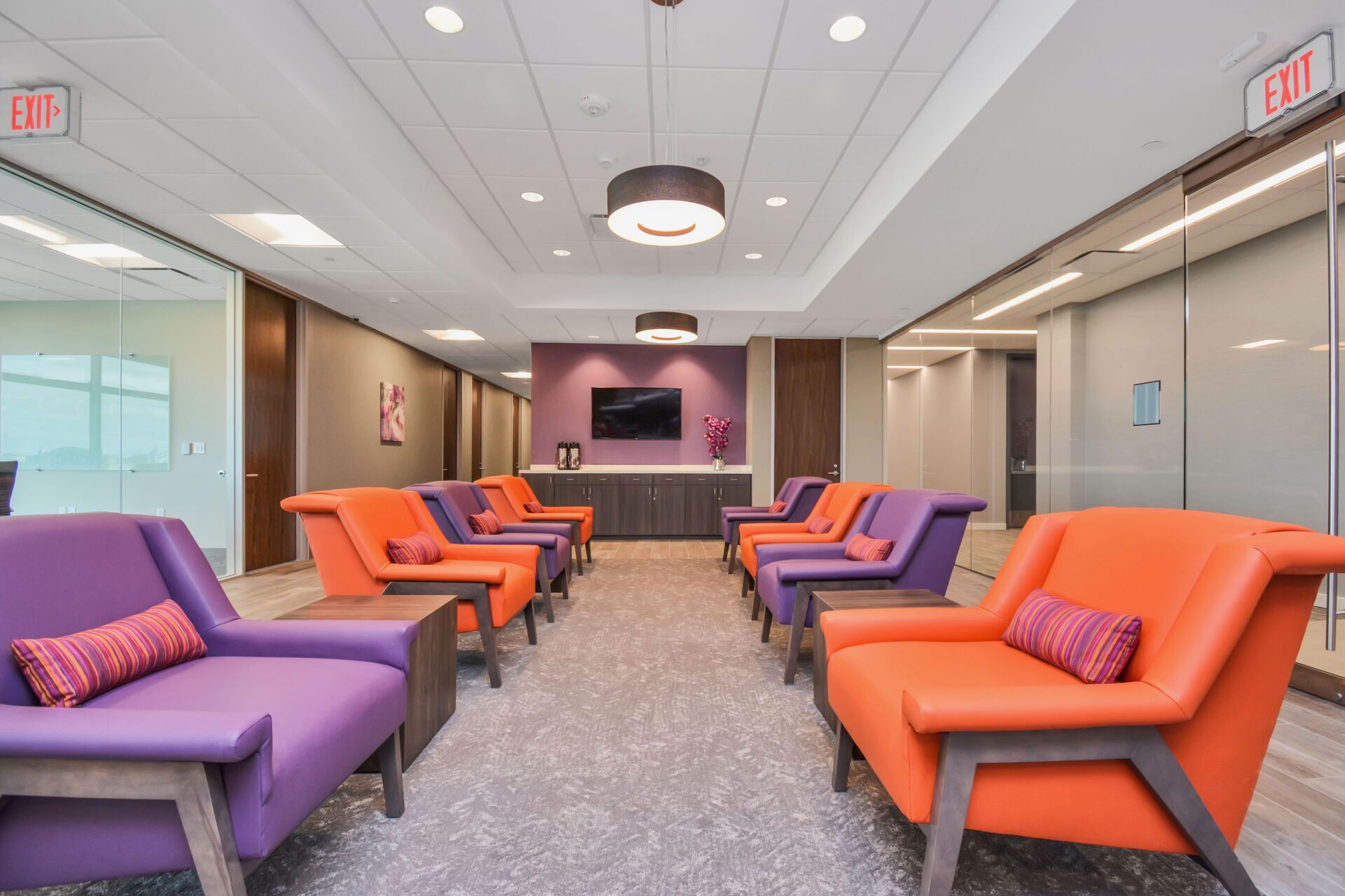 A waiting room with purple and orange chairs and an exit sign