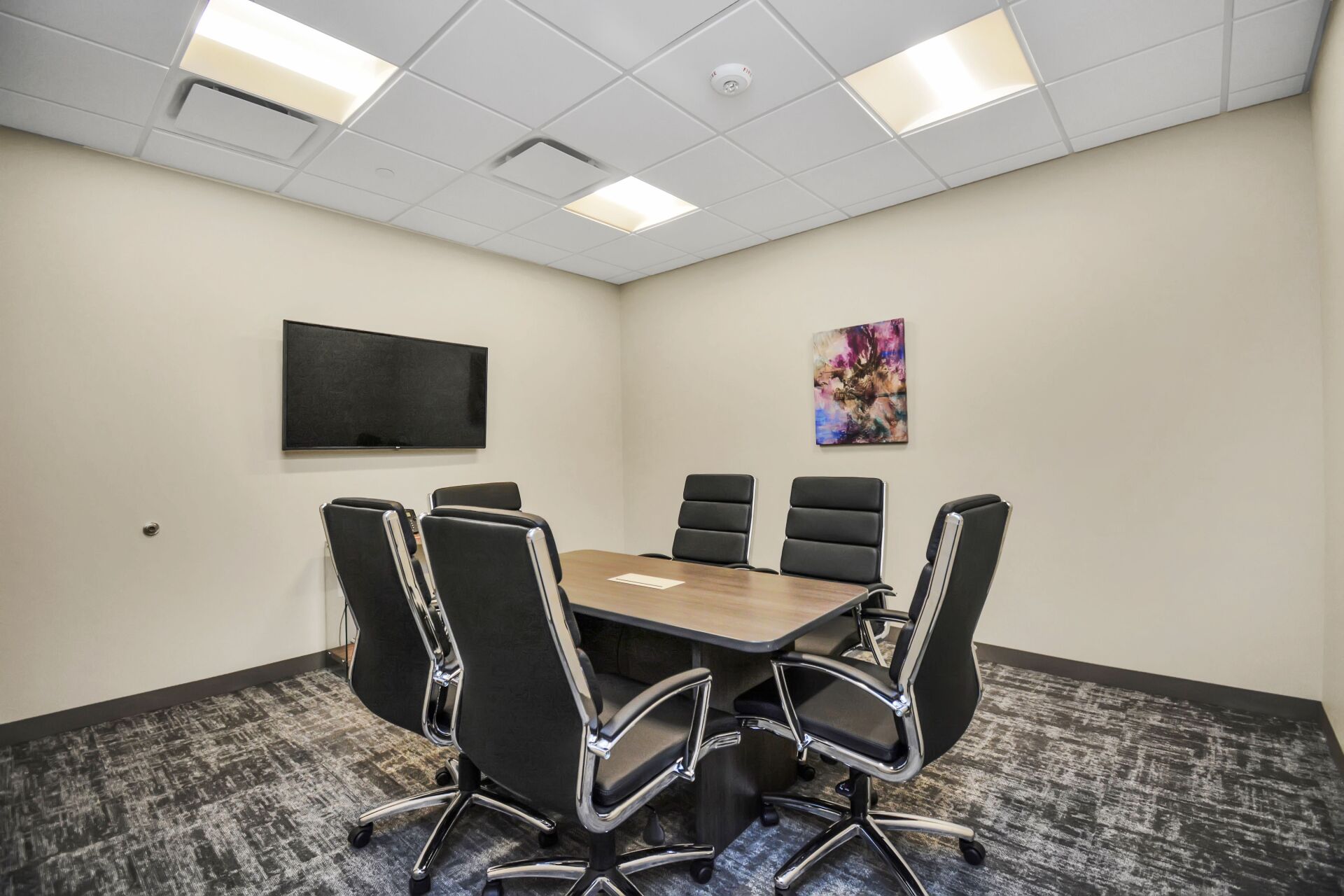 A conference room with a table and chairs and a flat screen tv.