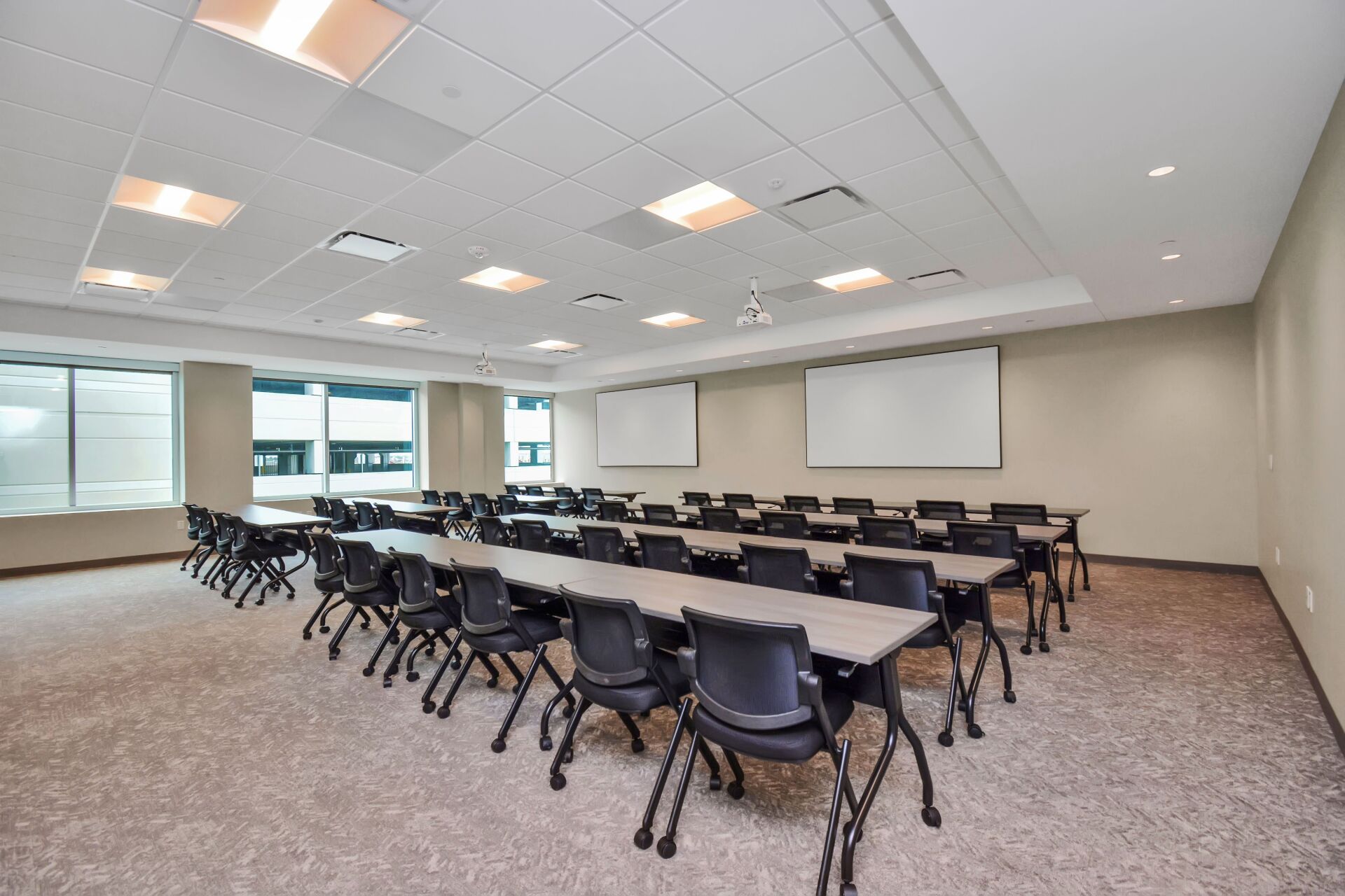 A large room with tables and chairs and a projector screen.