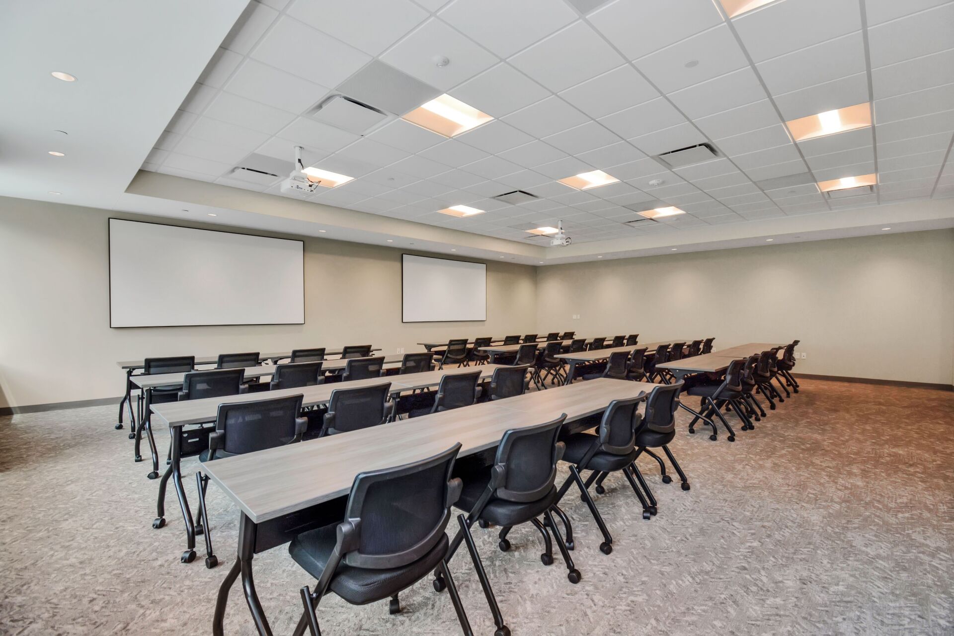 A large room with tables and chairs and a projector screen.