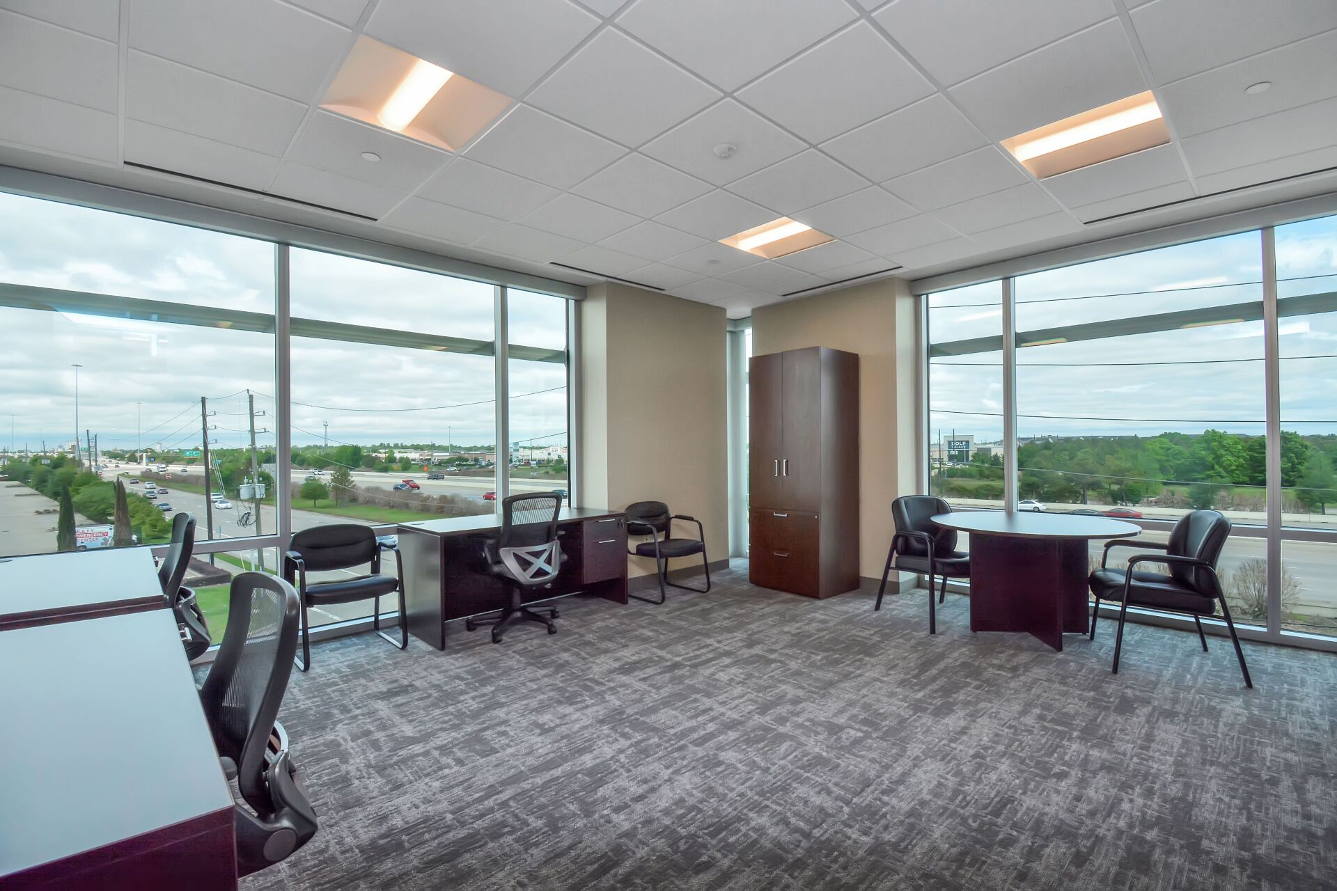 A large office with lots of windows and tables and chairs.