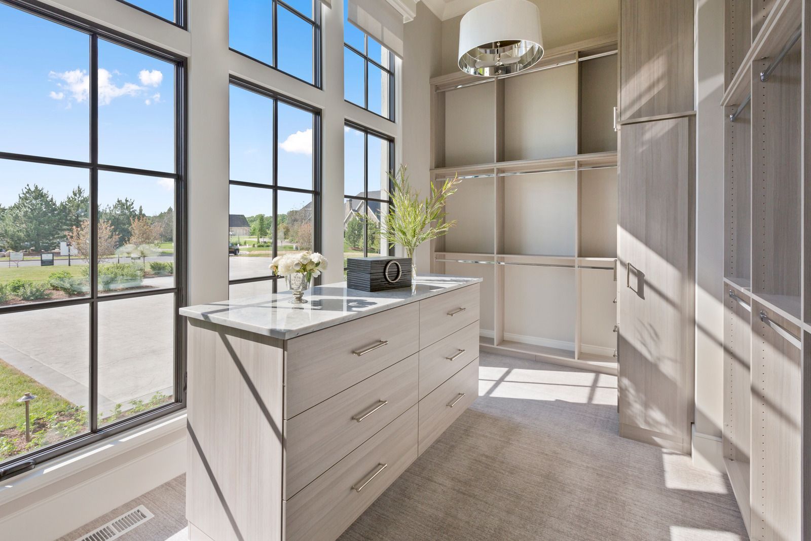 Bright modern walk-in closet with white cabinets, a central island, and large sunlit windows