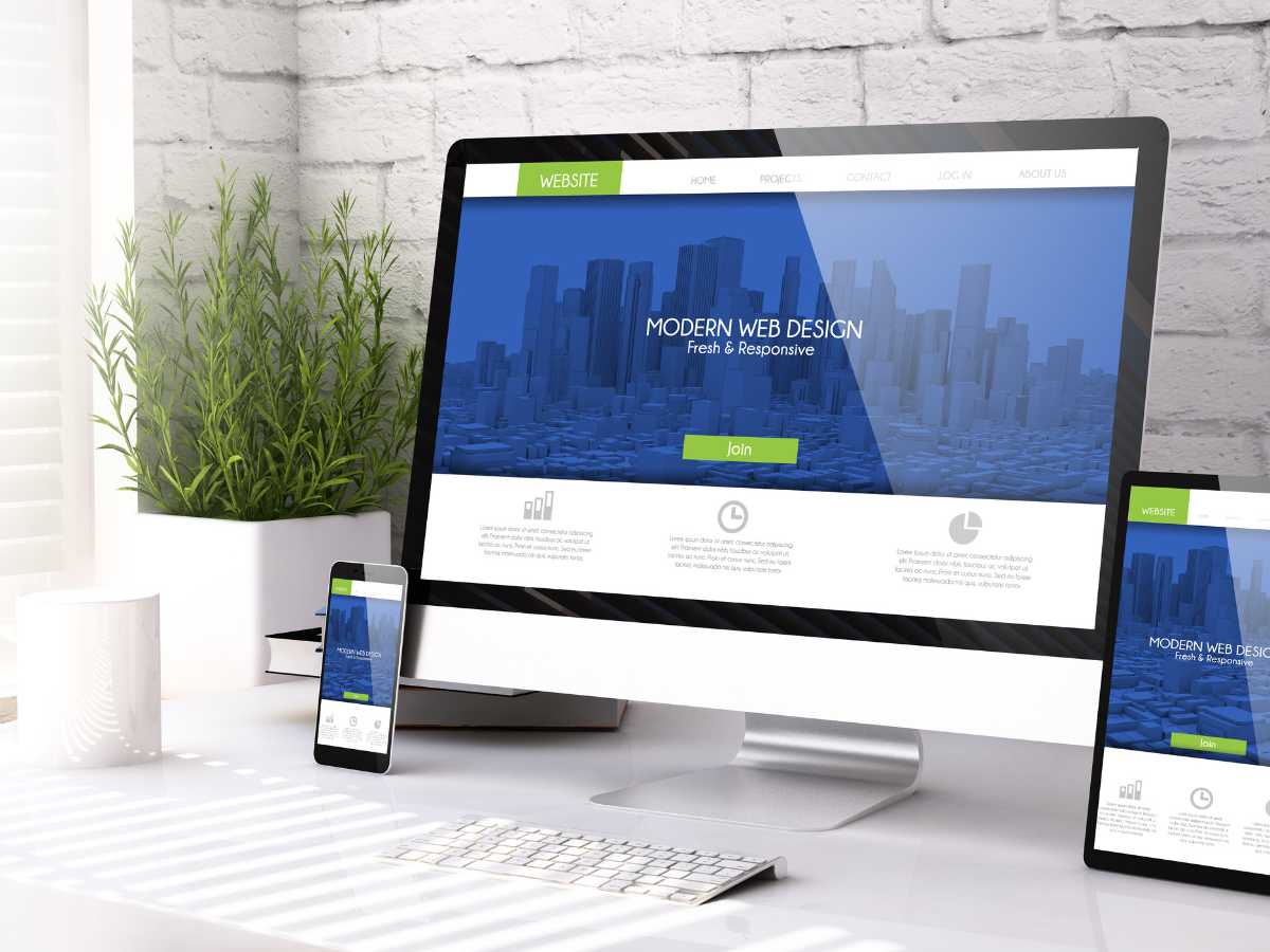 Desktop monitor, smartphone, and tablet showing a blue website mockup on a white desk.