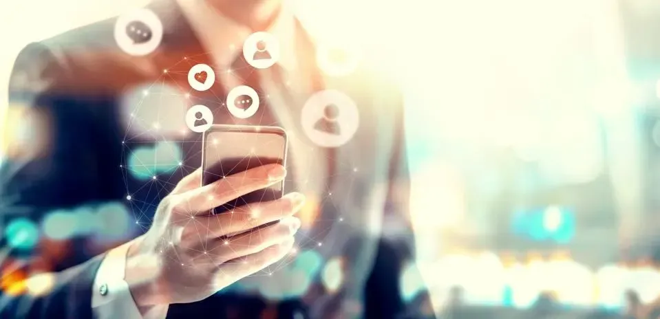 A man in a suit is holding a cell phone with social media icons coming out of it. A man in a suit is holding a cell phone with social media icons coming out of it.