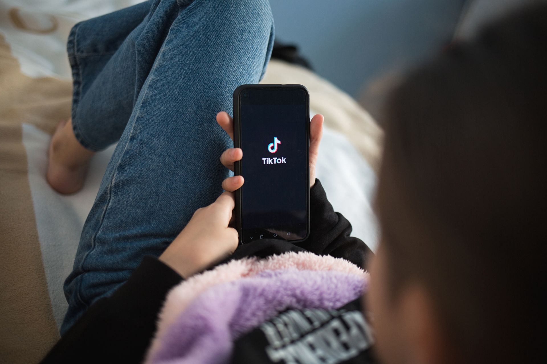 Person holding a phone with TikTok app on screen. Laying down, wearing jeans. Person holding a phone with TikTok app on screen. Laying down, wearing jeans.