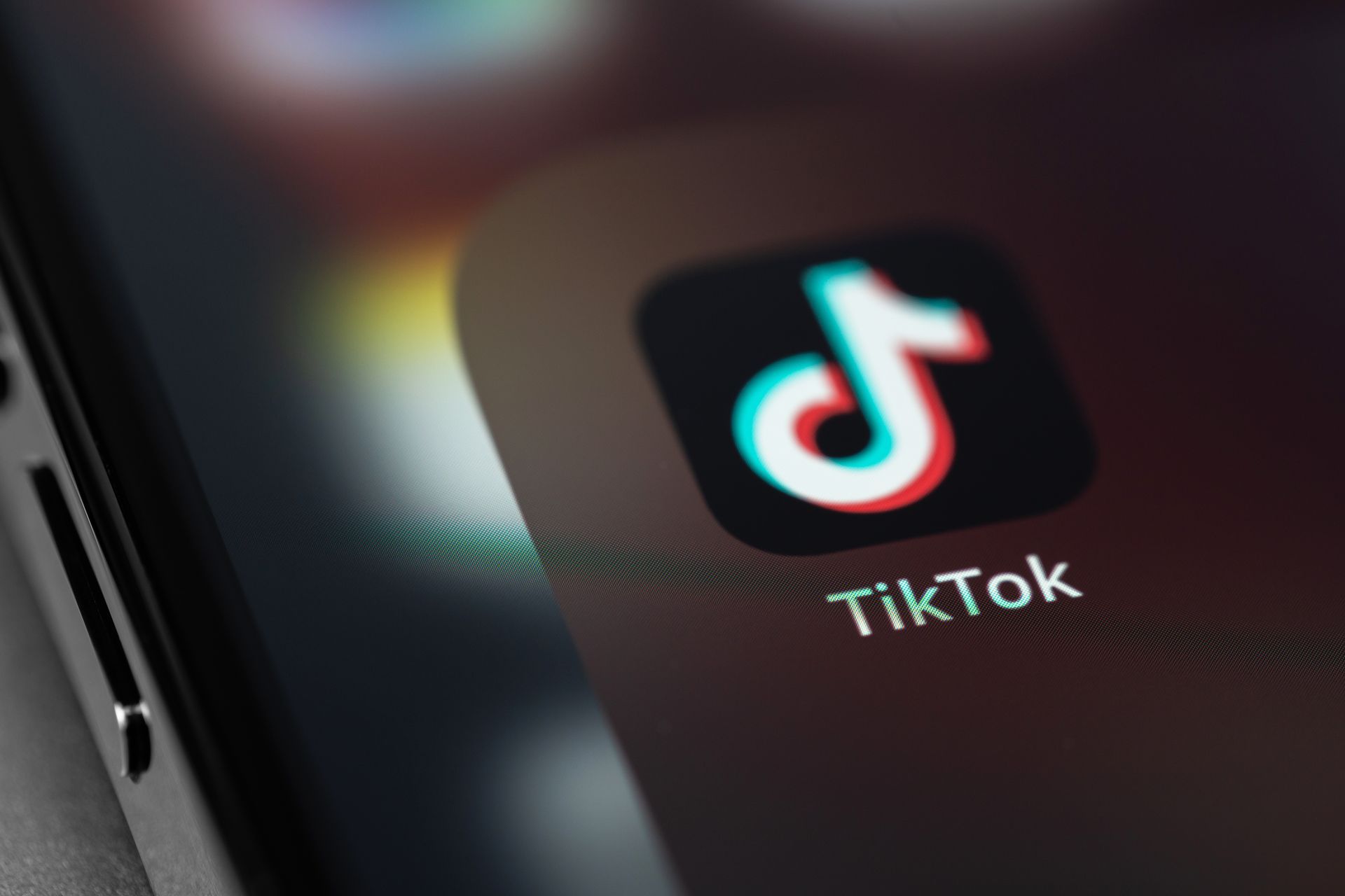 TikTok app icon on a smartphone screen, black background, white and red musical note logo. TikTok app icon on a smartphone screen, black background, white and red musical note logo.