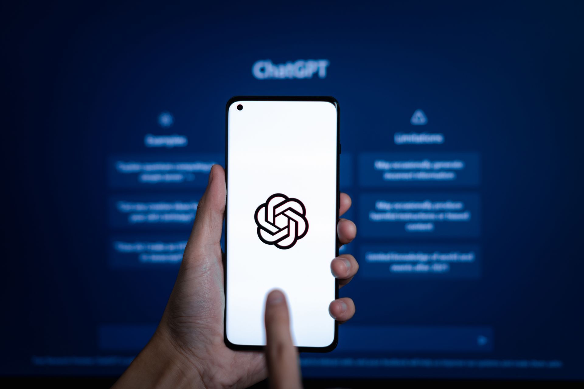 Hand holding a smartphone with the ChatGPT logo on a white screen against a blue ChatGPT background