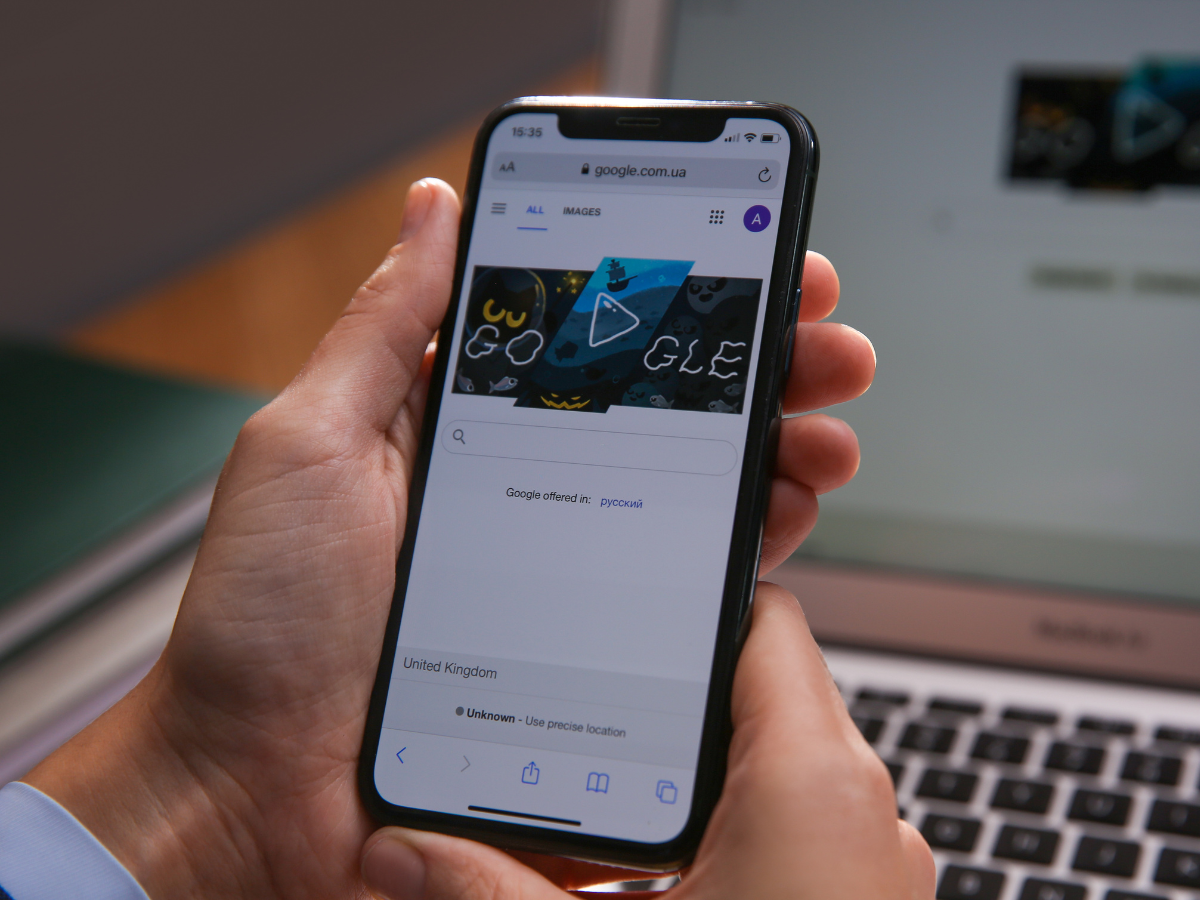 A person is holding a cell phone in front of a laptop.