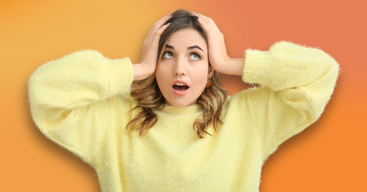 A woman in a yellow sweater is holding her head with her hands.