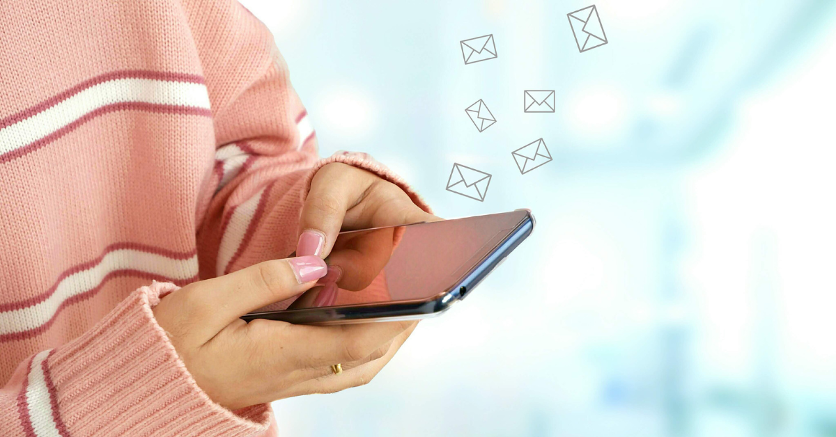 A woman in a pink sweater is holding a cell phone with envelope icons coming out of it.