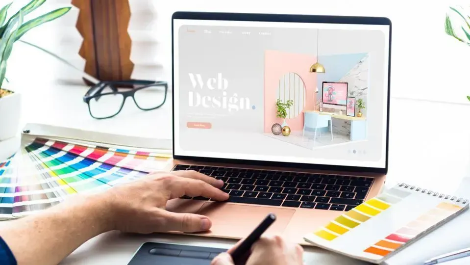 Someone designing a website using color swatches and a laptop. Someone designing a website using color swatches and a laptop.