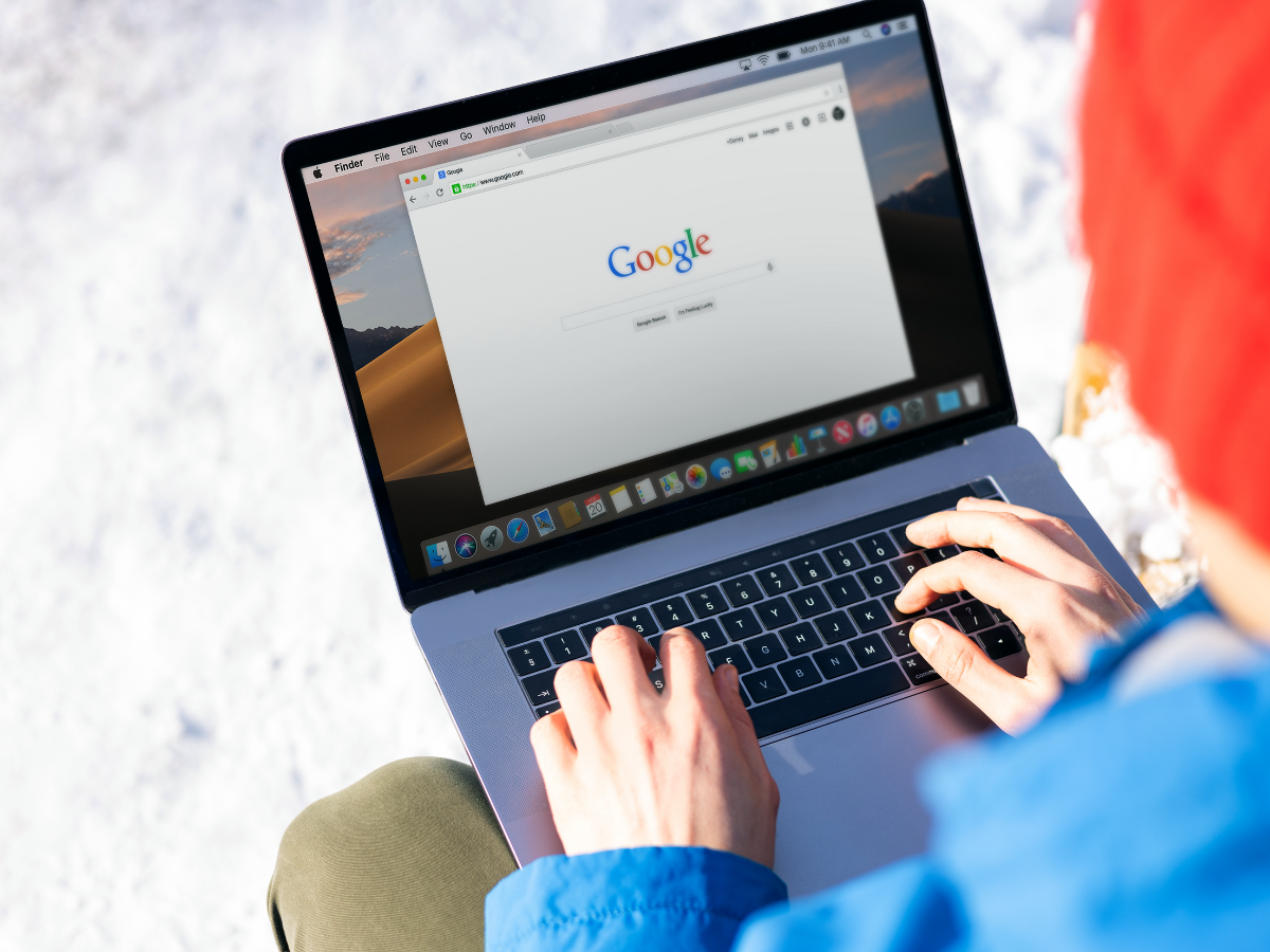 A person is typing on a laptop computer while sitting in the snow.