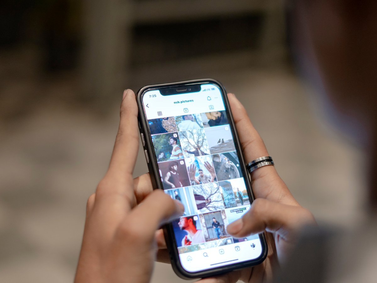 Person holding a smartphone, scrolling through a social media feed with photos; hands visible.