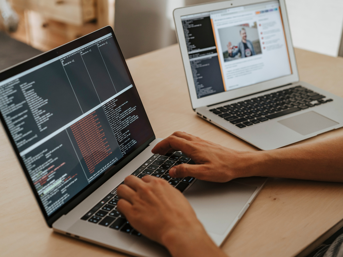 Person coding on a laptop; another laptop open with a webpage.