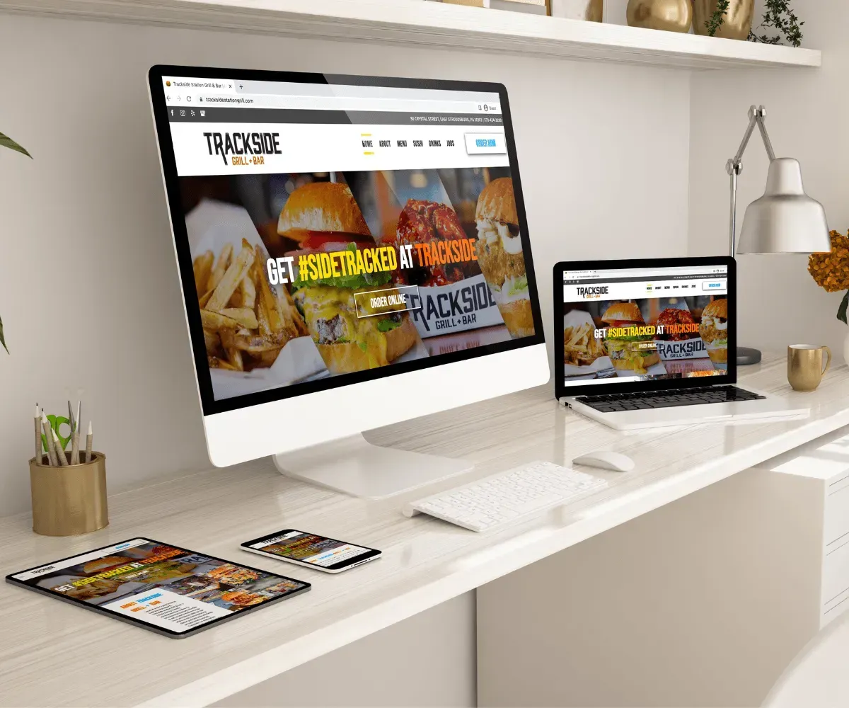Website design on various devices: desktop, laptop, tablet, and smartphone. Trackside Burgers website displayed.