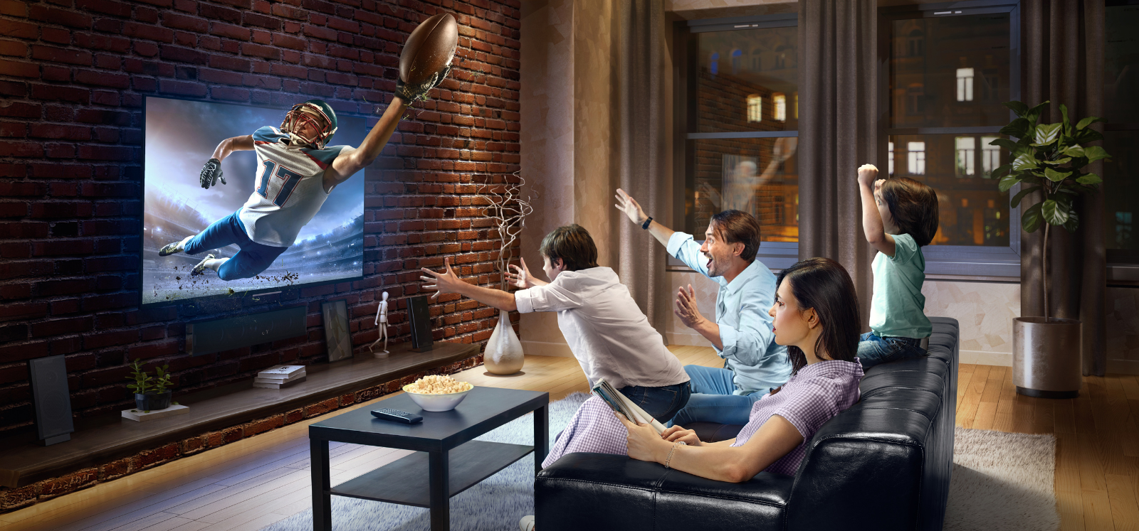 A family is sitting on a couch watching a football game on a television.