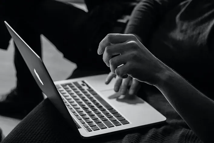 A person is typing on a laptop computer in a black and white photo.