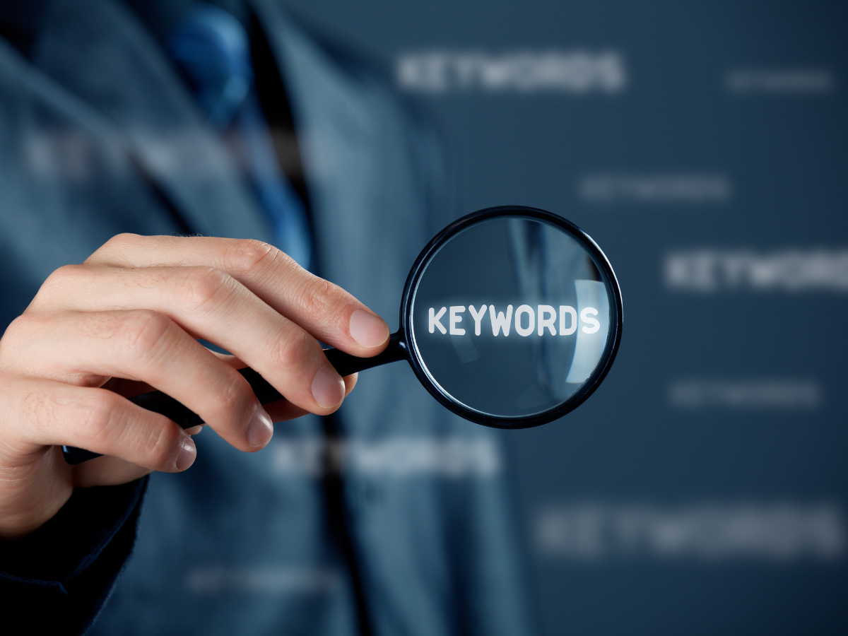 A person is holding a magnifying glass with the word keywords on it A person is holding a magnifying glass with the word keywords on it